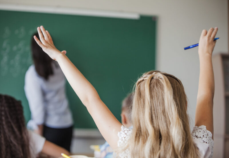 girl-sitting-classroom-raising-hands